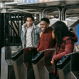 Three teenagers walking through NYC subway turnstiles at the same time, turned to one another in mid-conversation.
