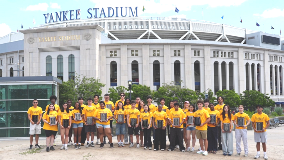 Group of over 30 high school-aged students holding award plaques and standing in front of Yankee Stadium
