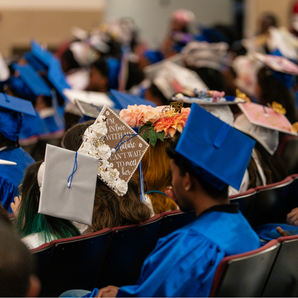 Back of students who are wearing blue graduation caps and gowns