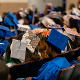 Back of students who are wearing blue graduation caps and gowns