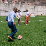 Chancellor Samuels getting ready to kick a soccer ball past two high school-aged students towards a goal.
