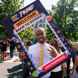 Chancellor Samuels smiling while holding a giant frame around his upper torse that reads, "NYC Public Schools Proud, welcome back to school, #NYCPSProud'