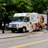 Side view of a large van with signage for NYCPS' Childcare for All program. 'Apply to 2-K' is spelled out in large letters alongside an image of a young child.