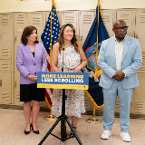 Governor Kathy Hochul (left), Chancellor Melissa Aviles-Ramos (center), and Mark Rampersant, chief of school safety (right), are standing at a podium together with a banner that reads, "More Learning Less Scrolling."