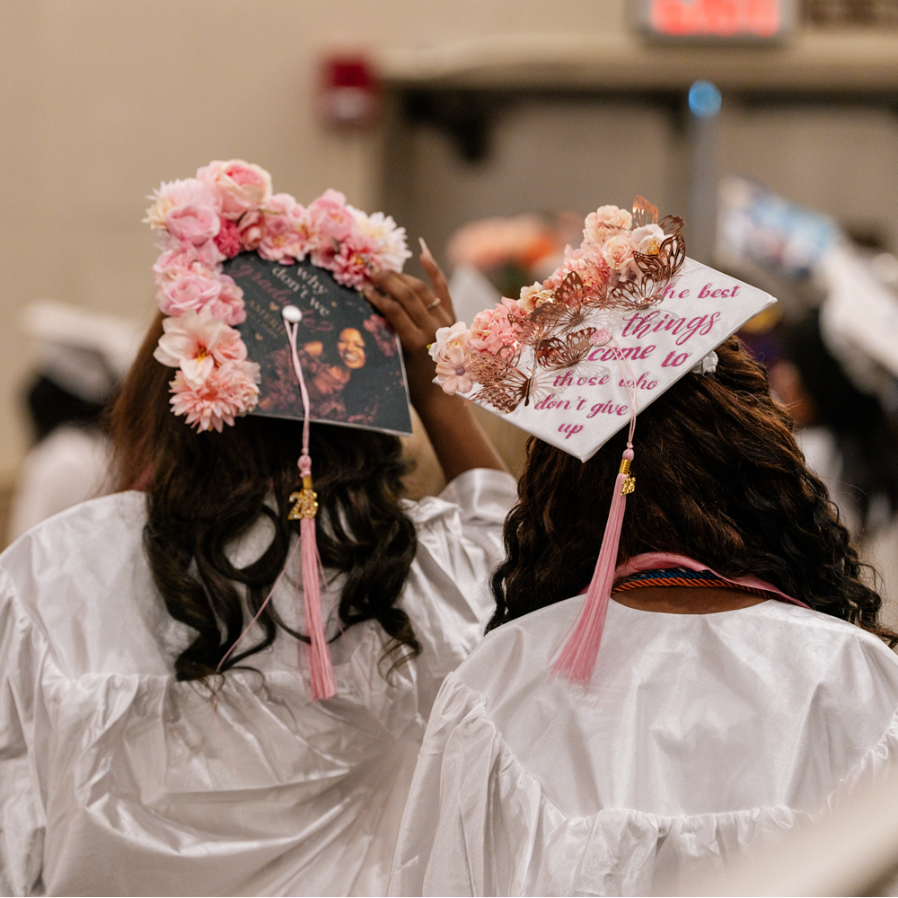 Rear view of a pair of high school students in white graduation caps and gowns.