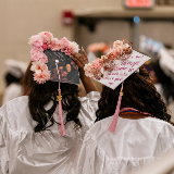 Rear view of a pair of high school students in white graduation caps and gowns.