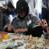 A student wearing rain gear is painting at a table.
