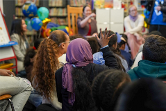 Behind-the-back shot of a class of young students sitting on a carpet waiting for storytime to begin.