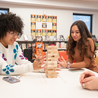 Two students sitting at a table in a library playing Jenga together.