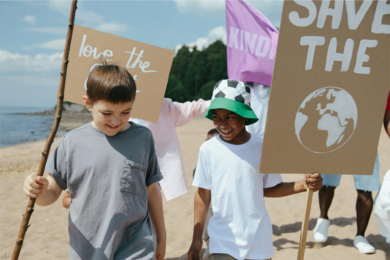 Two young elementary-aged students on a beach holding up pro-environmental signs like, 