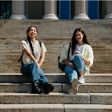 Two teenaged girls sitting on a set of court stairs.