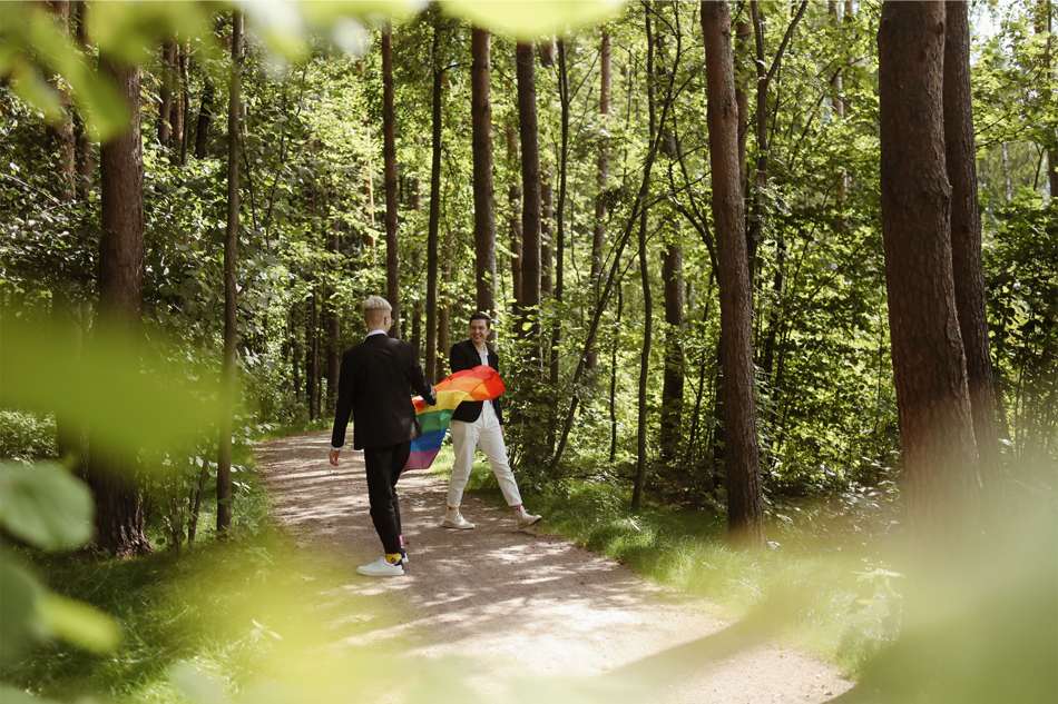 Two young men walking in a park with a rainbow-colored pride flag