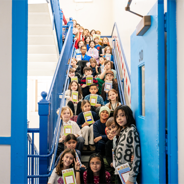 Shot of several elementary school-aged students sitting on a school stairway while holding books in their hands.