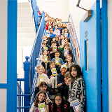 Shot of several elementary school-aged students sitting on a school stairway while holding books in their hands.