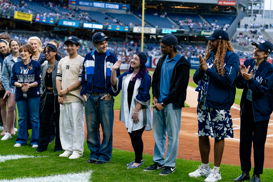 2025's Yankees Stonewall Scholarship winners standing near home plate at Yankee Stadium alongside several executives from the Yankees, Stonewall Inn, and NYC Public Schools