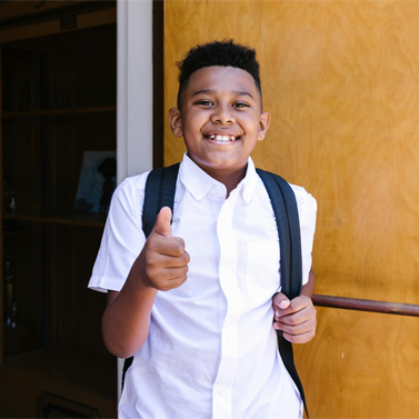Elementary school-aged student smiling and pointing at camera